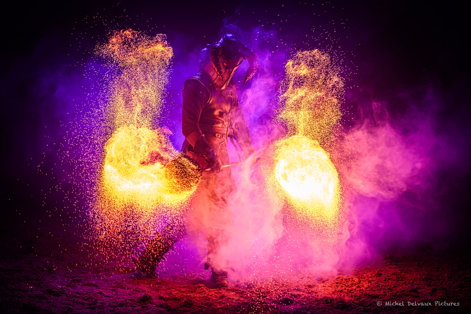 Nemesis : artiste avec deux éventails de feu, parmi les étincelles et la fumée violette.